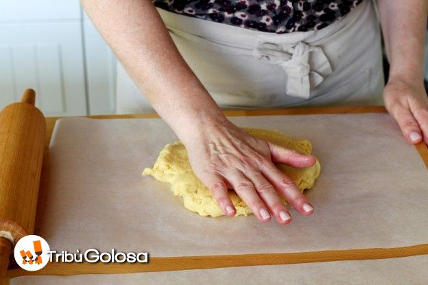 Mettete la pasta su un foglio di carta da forno e schiacciatela con la mano in modo da darle una forma circolare